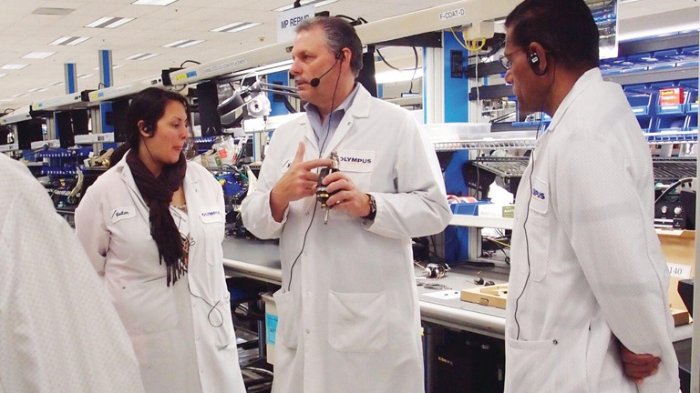 Training and employee well-being are critical to Olympus  Corp. of America’s success. Mike Jensen (center) engages engineers, trainers and trainees on the plant floor.  (Provided by Olympus of America)